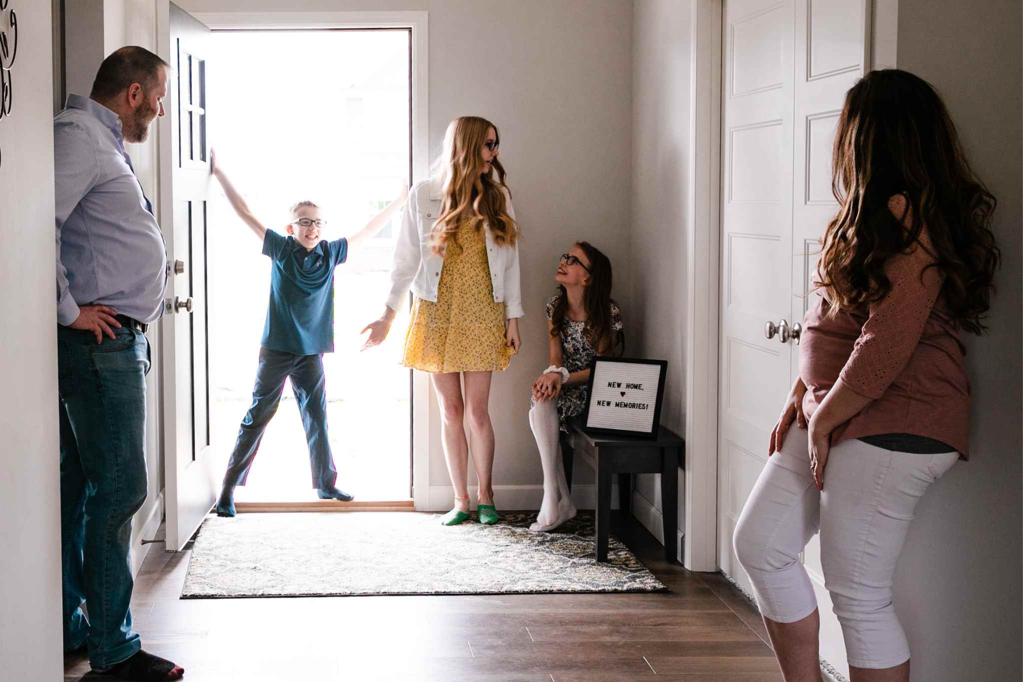 Family celebrating in a new home entryway, with a boy joyfully welcoming others, women seated with a sign reading "New Home, New Memories!"
