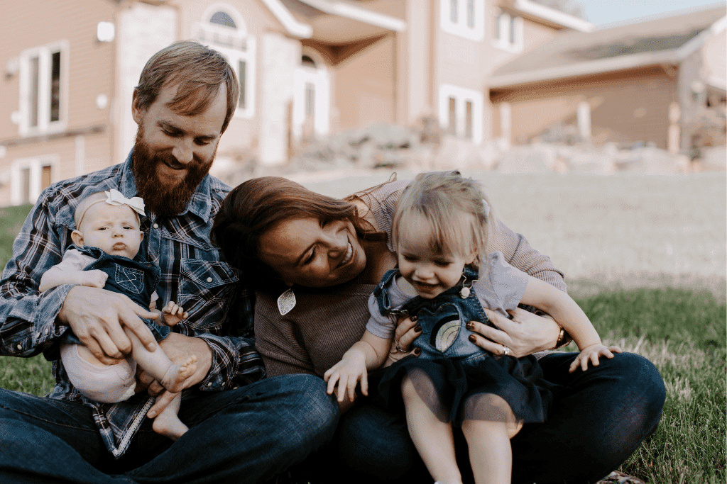 Family enjoying time outdoors, father holding baby, mother interacting with toddler, showcasing warmth and togetherness in a home setting.