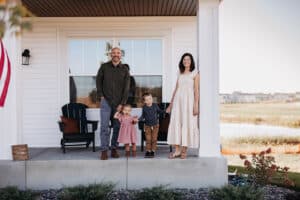 Family standing on the porch of a home, smiling, with a scenic background, representing the benefits of homeownership and potential cash-out refinancing options.